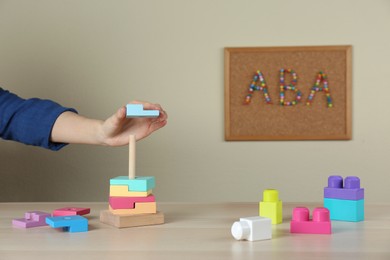 Photo of Child playing with toy pyramid at wooden table indoors, closeup. ABA therapy concept