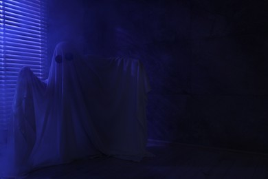 Creepy ghost. Woman covered with sheet near window in blue light, space for text