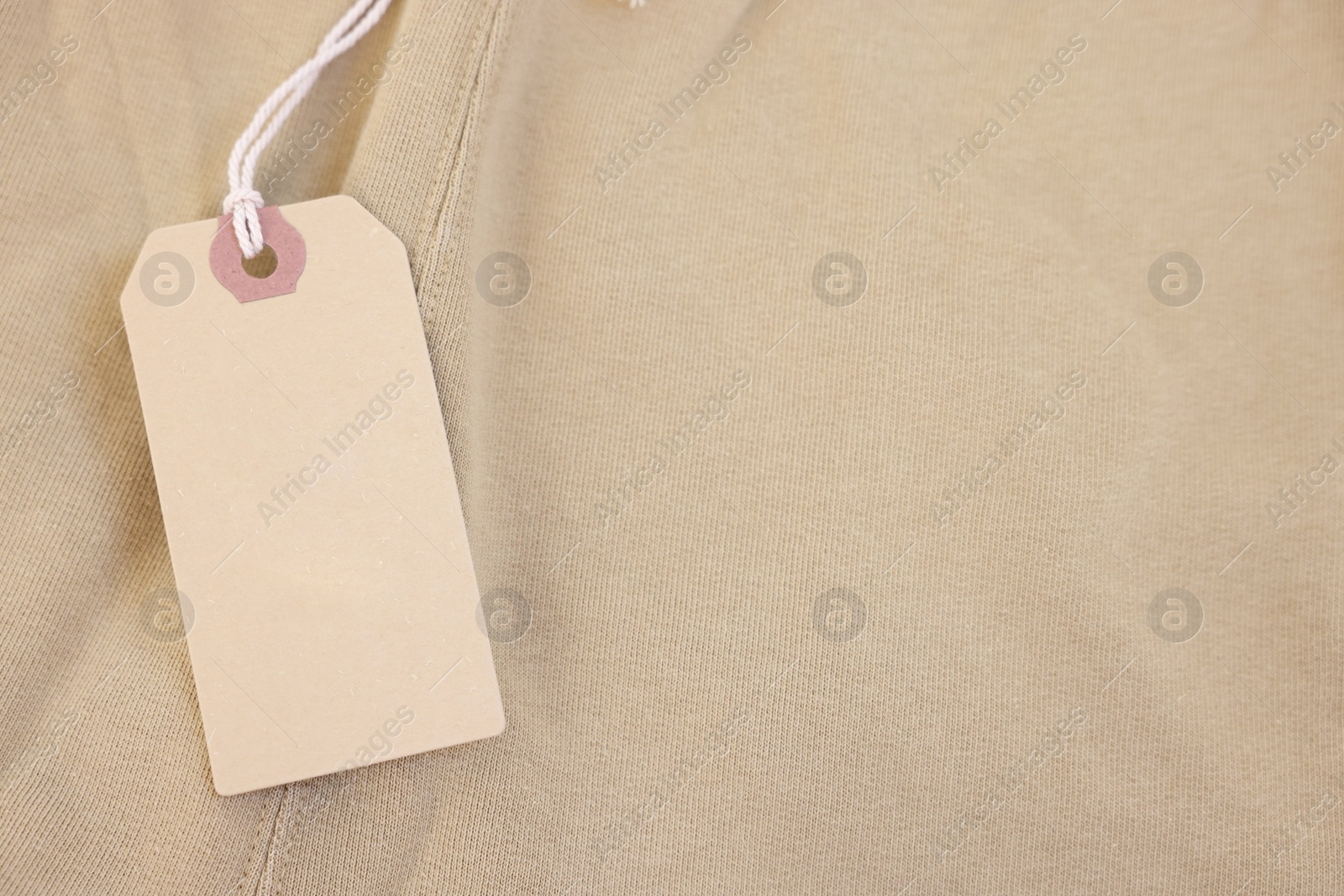 Photo of Cardboard tag on beige garment, top view. Space for text