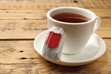 Photo of Tea bag and cup of hot beverage on wooden table, closeup. Space for text
