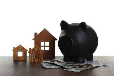 Photo of Piggy bank, house models and dollar banknotes on wooden table against white background. Saving money concept