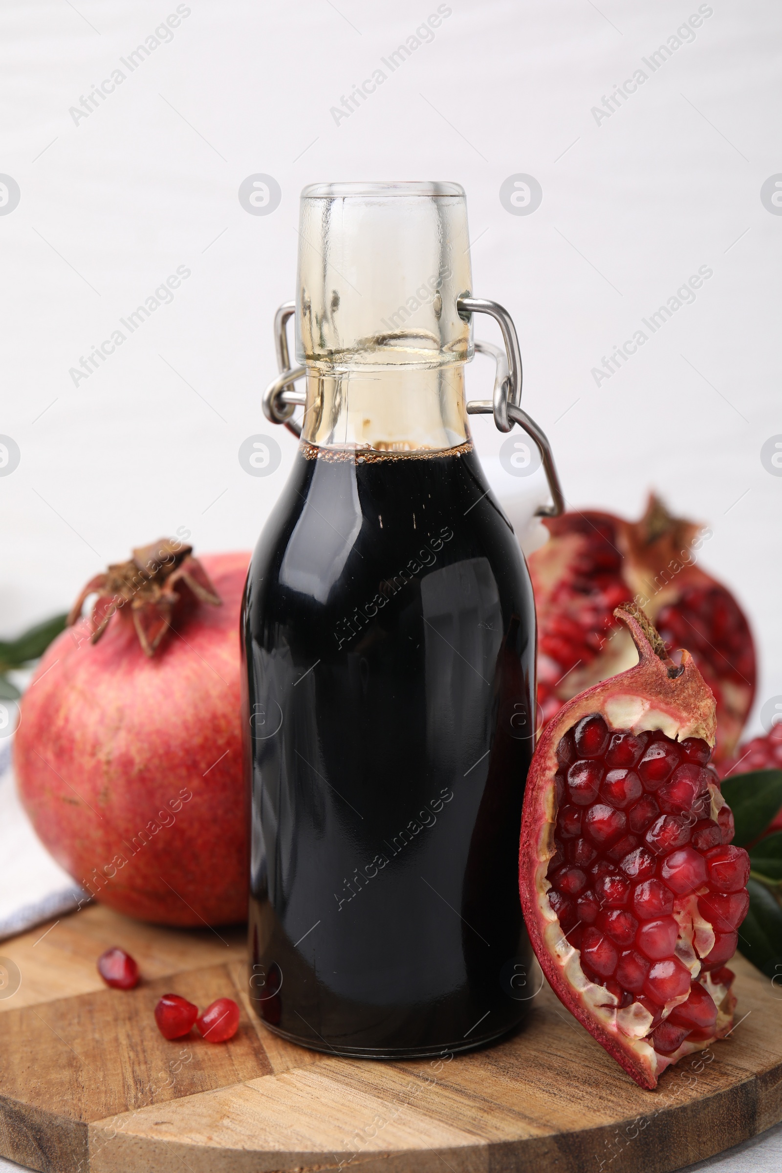 Photo of Tasty pomegranate sauce in bottle and fruits on light table, closeup