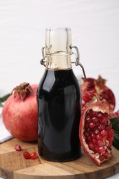 Photo of Tasty pomegranate sauce in bottle and fruits on light table, closeup