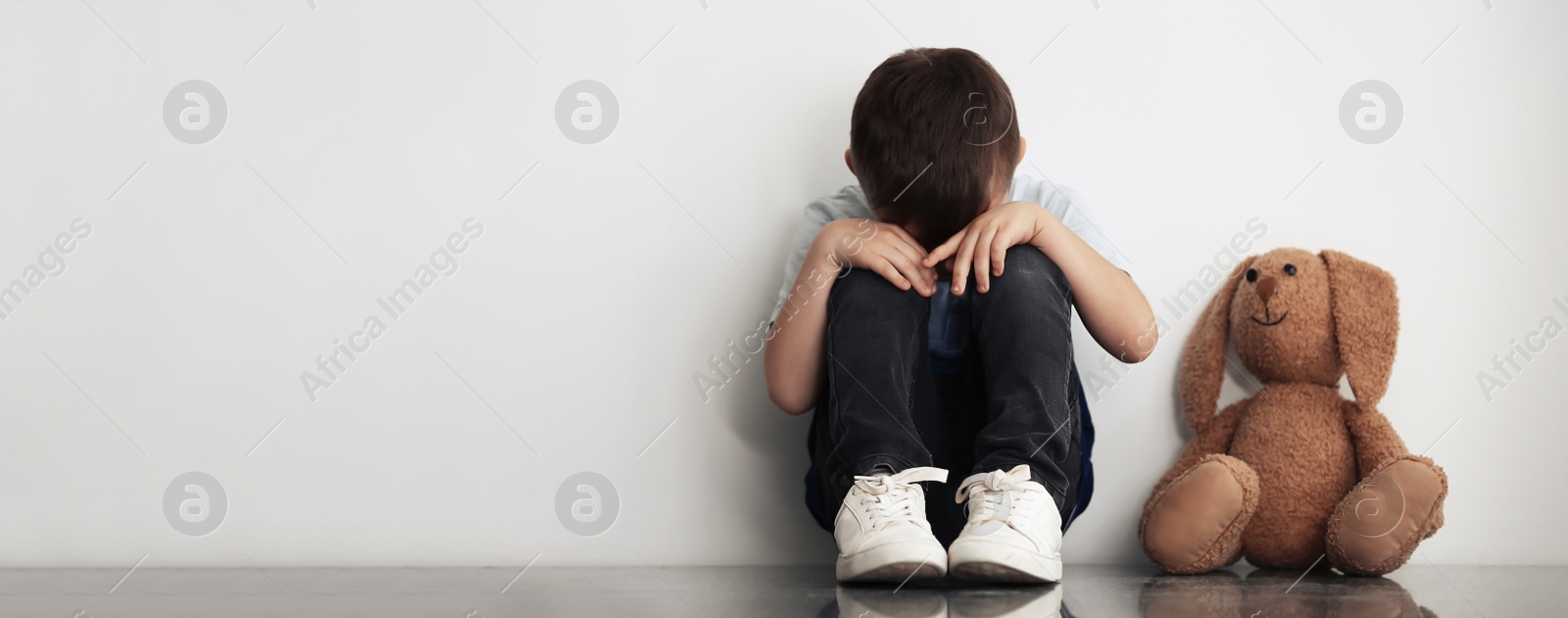 Image of Sad little boy sitting near white wall, banner design with space for text. Time to visit child psychologist