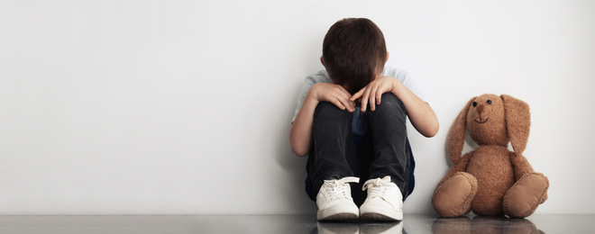 Image of Sad little boy sitting near white wall, banner design with space for text. Time to visit child psychologist