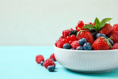 Photo of Mix of different fresh berries and mint in bowl on light blue wooden table. Space for text