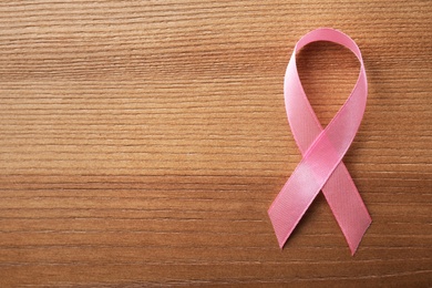 Photo of Pink ribbon on wooden background, top view with space for text. Breast cancer awareness concept