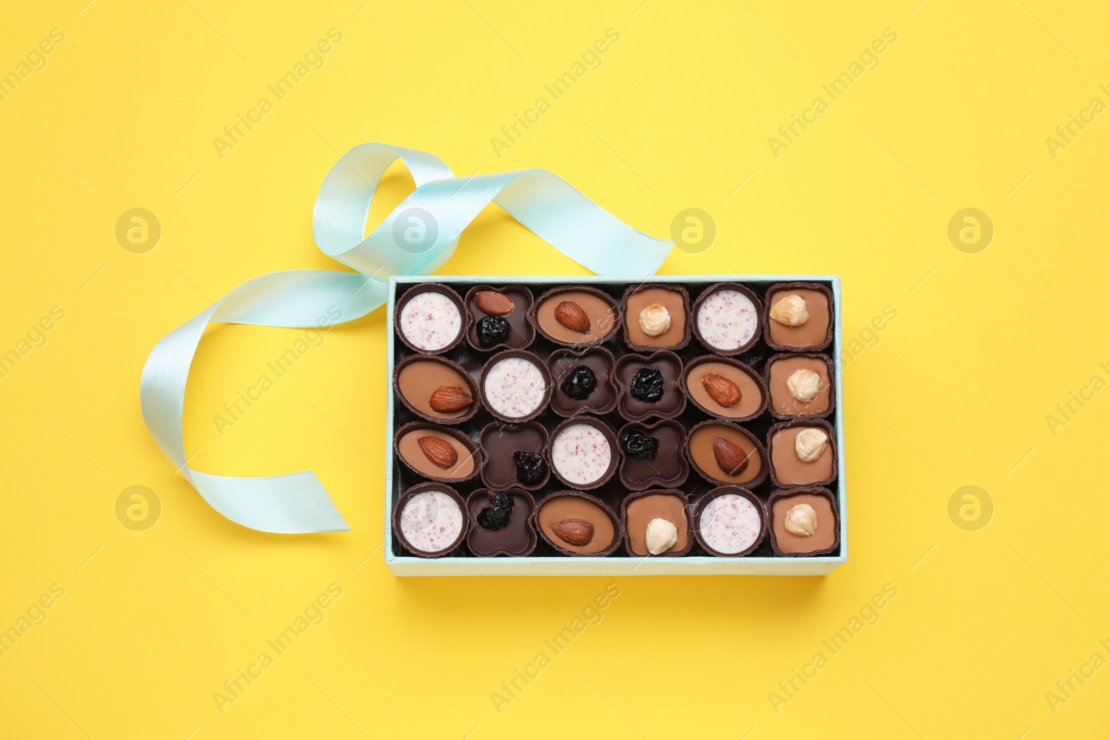 Photo of Box of delicious chocolate candies on yellow background, top view