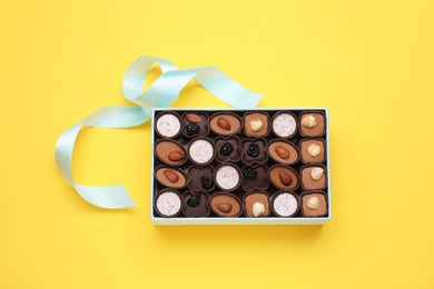 Photo of Box of delicious chocolate candies on yellow background, top view