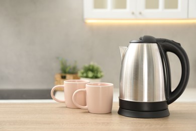 Photo of Modern electric kettle and cups on table in kitchen. Space for text