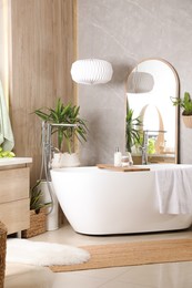 Photo of Modern white tub and beautiful green houseplants in bathroom. Interior design