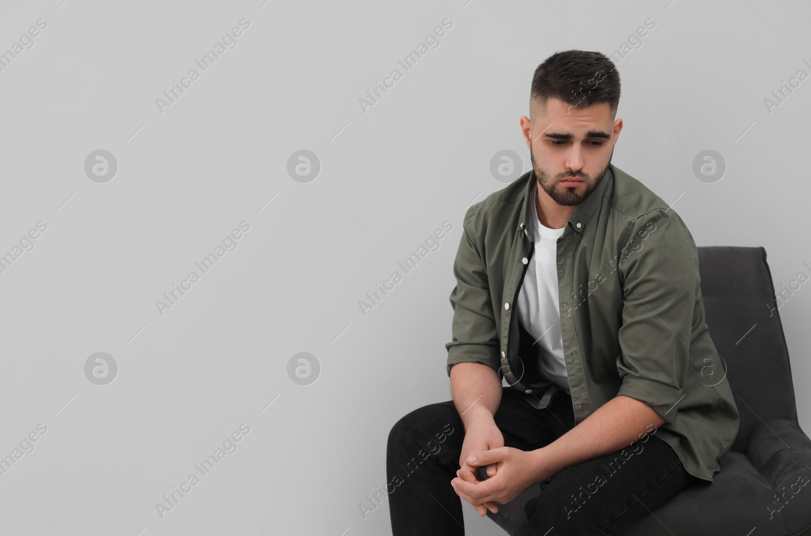 Photo of Sad man sitting near light grey wall. Space for text