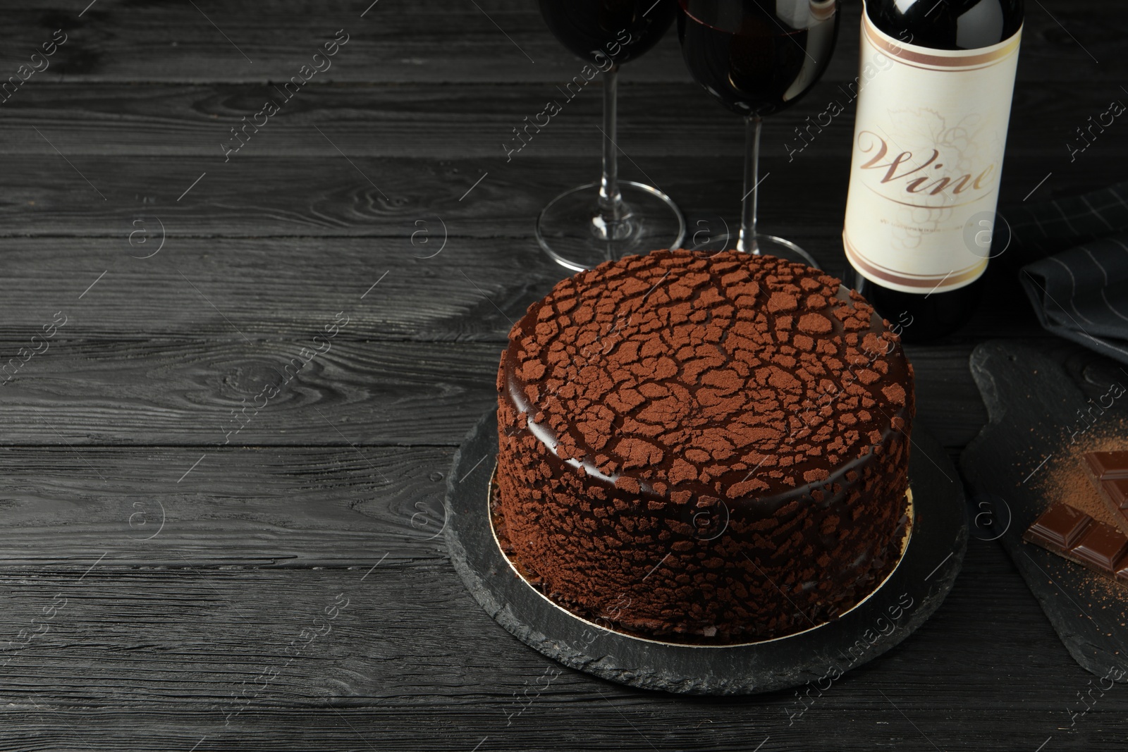 Photo of Delicious truffle cake, chocolate pieces and red wine on black wooden table, space for text