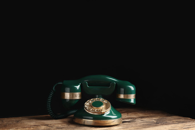 Photo of Vintage corded phone on wooden table against black background. Space for text