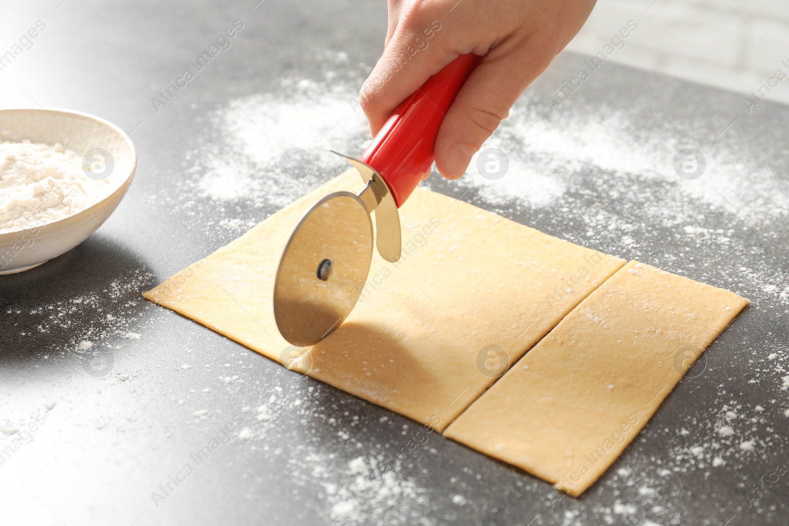 Photo of Young woman cutting dough for pasta on table