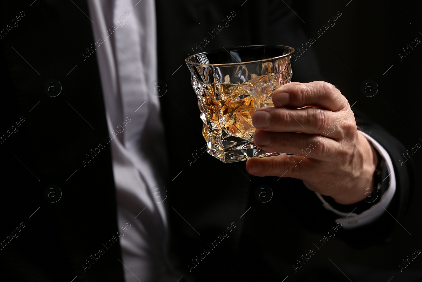 Photo of Man holding glass of whiskey with ice cubes on dark background, closeup