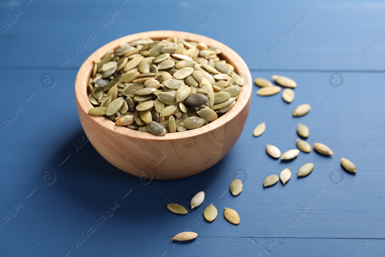 Photo of Bowl with peeled pumpkin seeds on blue wooden table