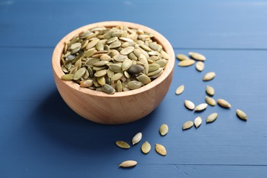 Bowl with peeled pumpkin seeds on blue wooden table