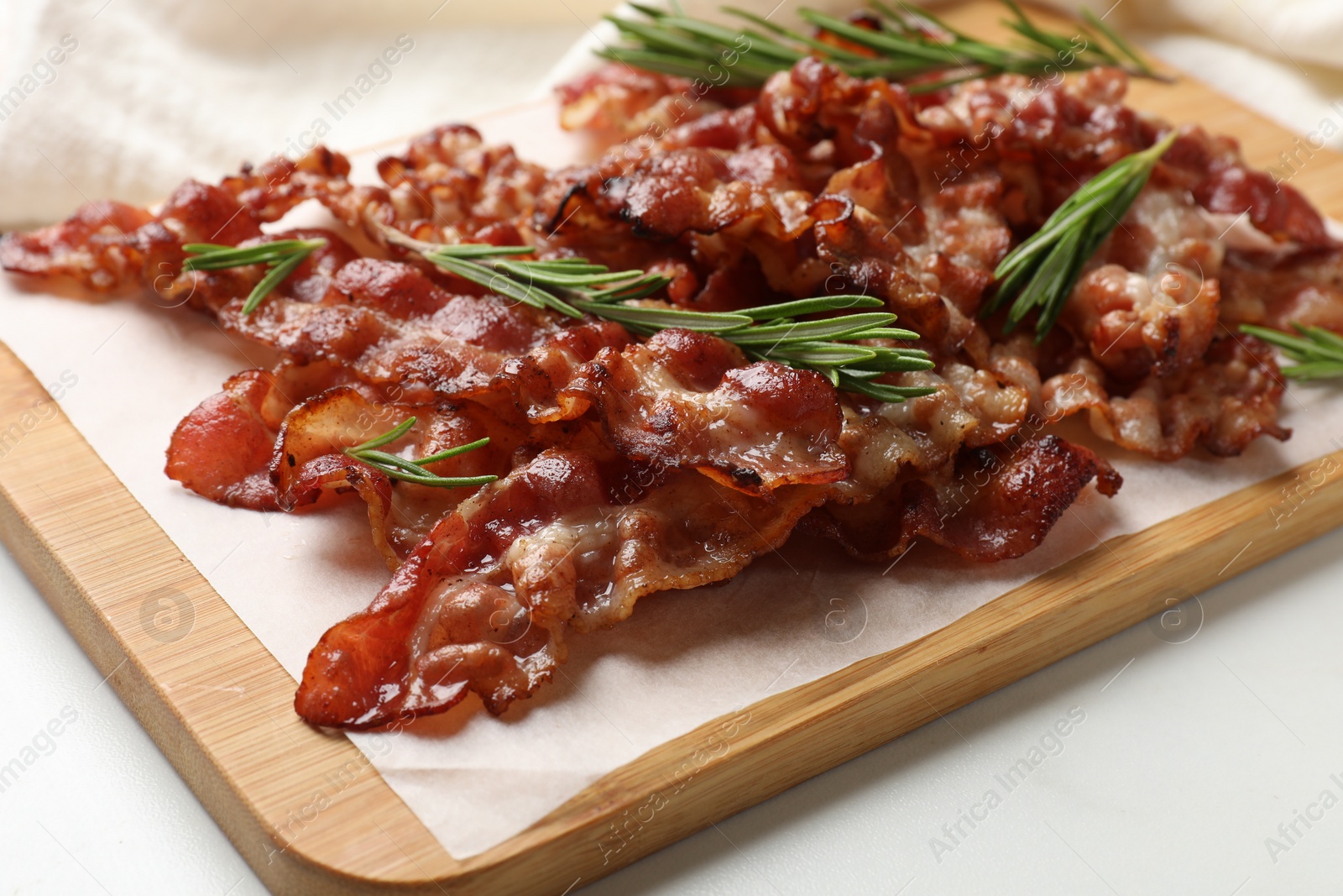 Photo of Slices of tasty fried bacon with rosemary on white table, closeup