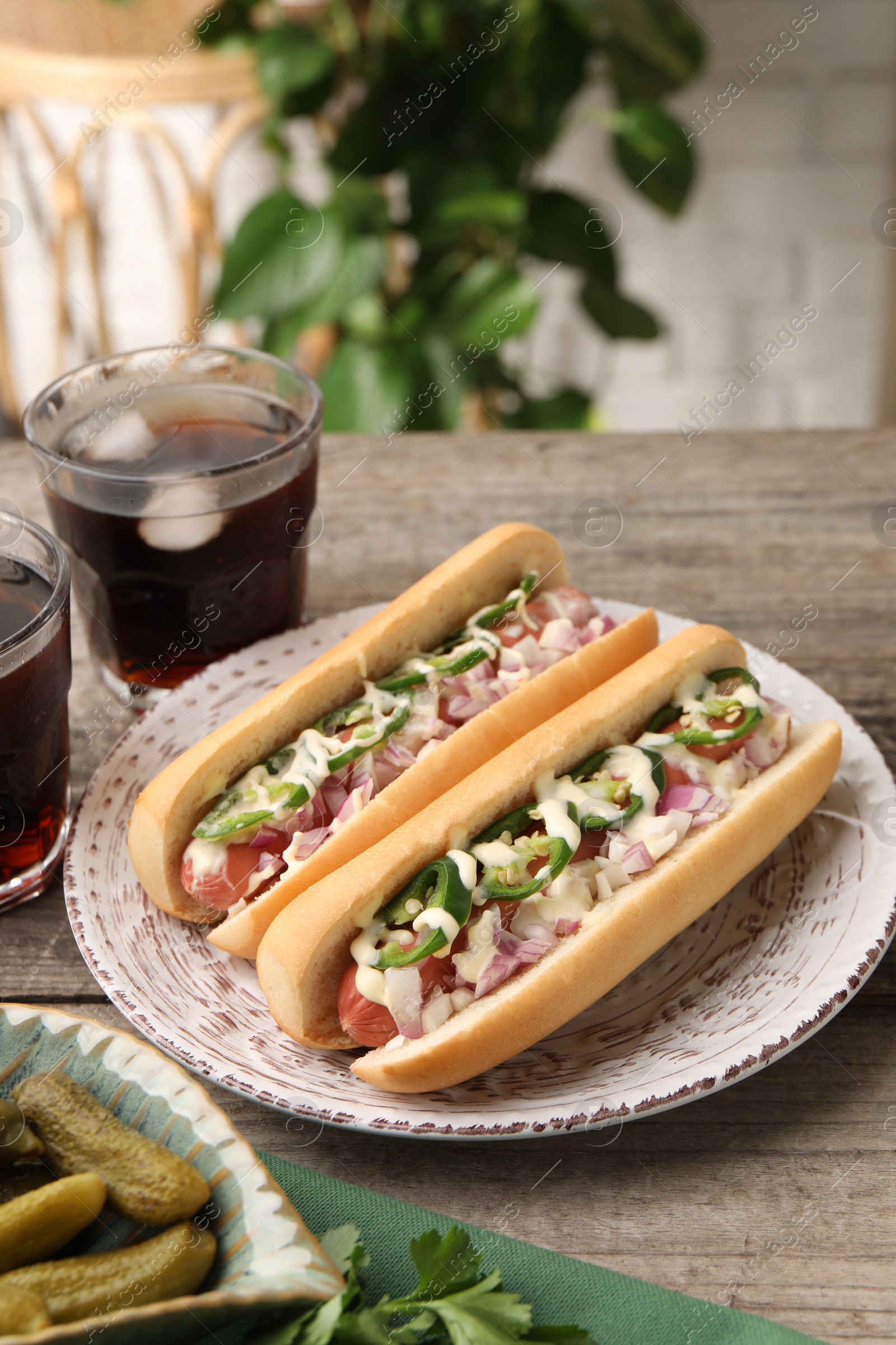 Photo of Delicious hot dogs with onion, chili pepper and sauce served on wooden table