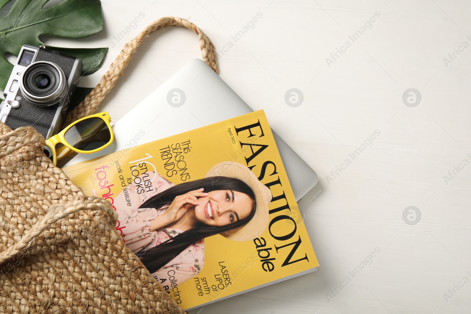 Photo of Bag with fashion magazine, laptop and camera on white wooden table, above view. Space for text