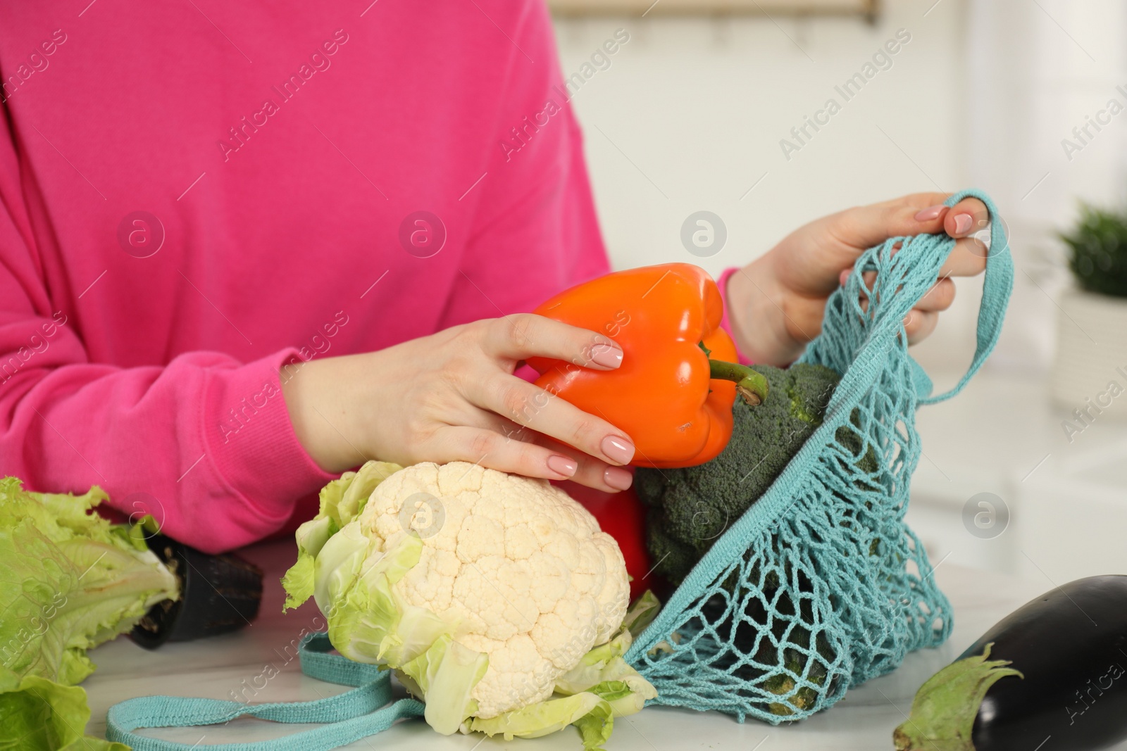 Photo of Woman taking pepper out from string bag at light marble table, closeup