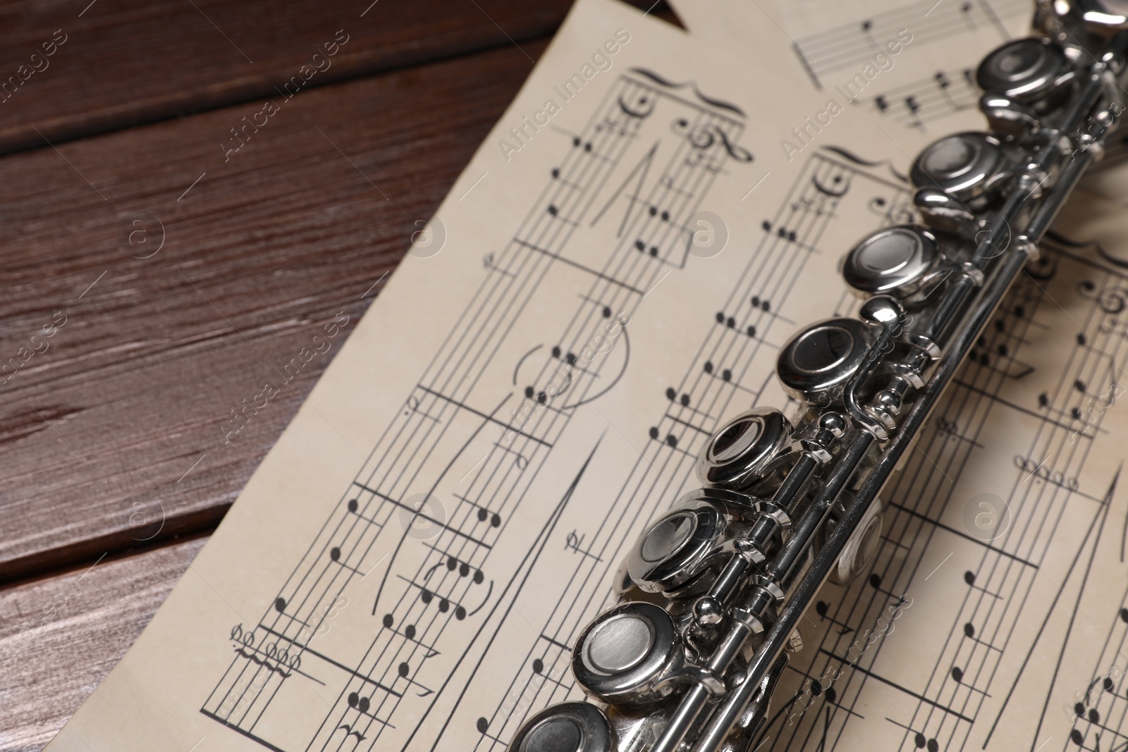 Photo of Sheets with musical notes and flute on wooden table, closeup