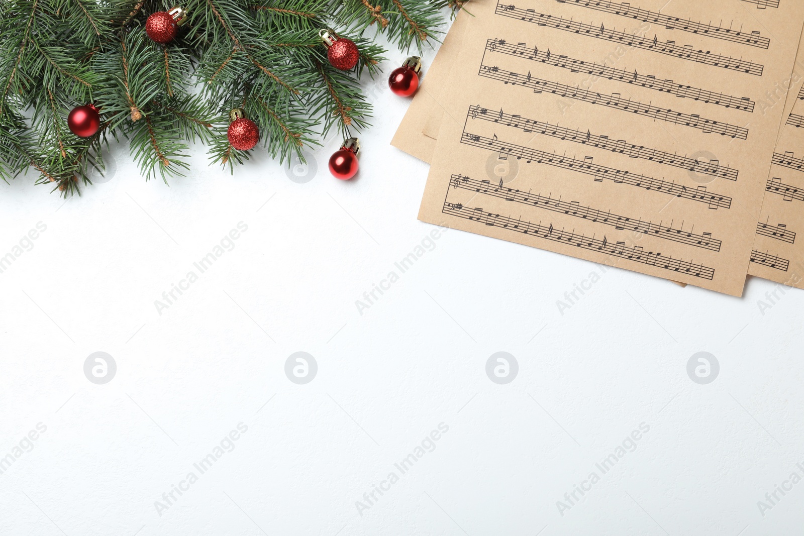 Photo of Music sheets near fir tree branches with Christmas balls and space for text on white background, flat lay