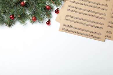 Music sheets near fir tree branches with Christmas balls and space for text on white background, flat lay