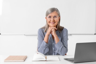 Photo of Happy professor sitting near laptop at desk in classroom
