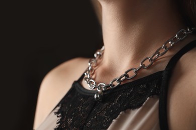 Photo of Woman wearing stylish metal chain with pendant on black background, closeup. Luxury jewelry