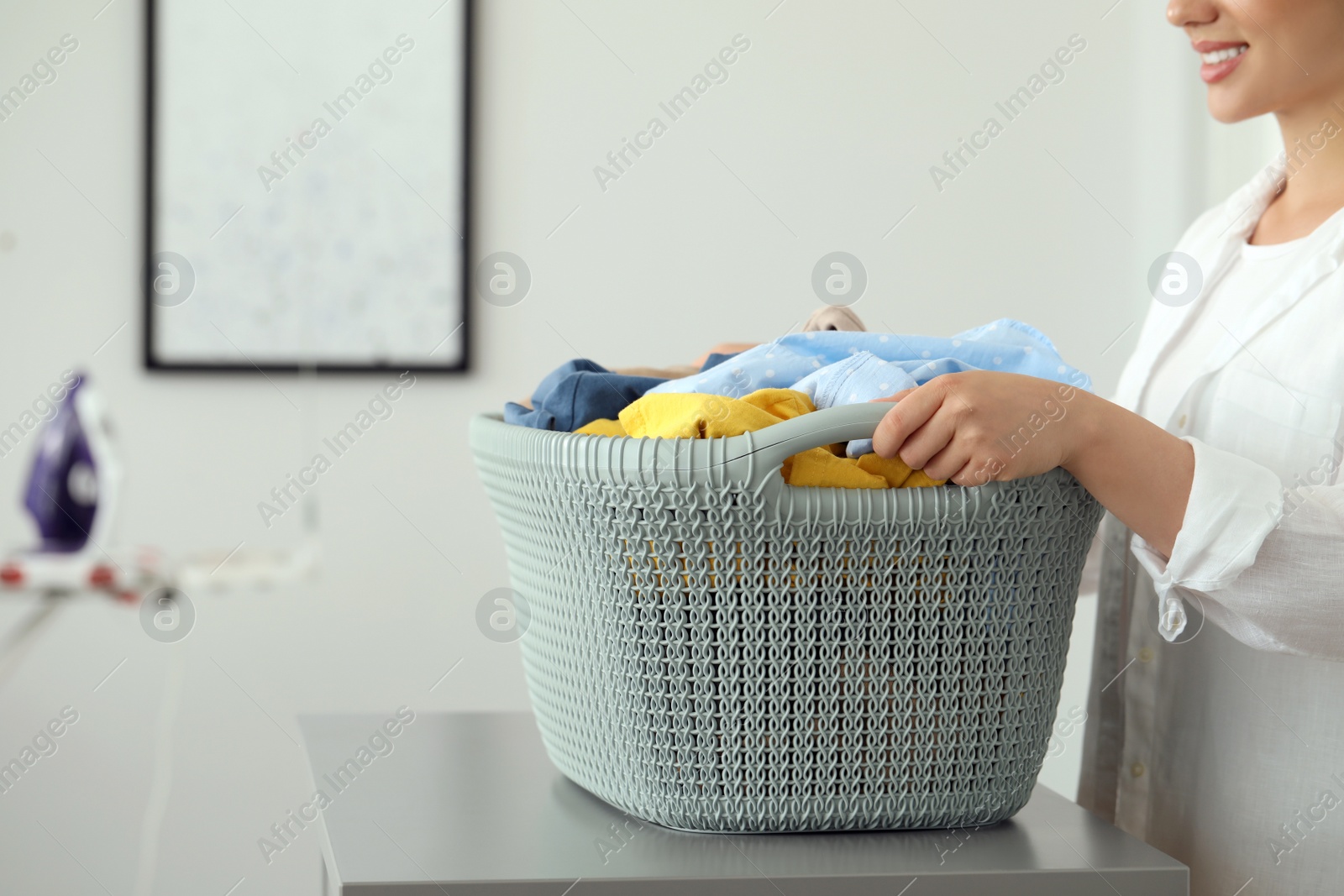 Photo of Woman with basket full of clean laundry at grey table indoors, closeup