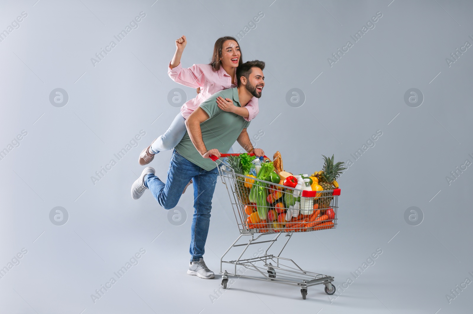 Photo of Young couple with shopping cart full of groceries on grey background