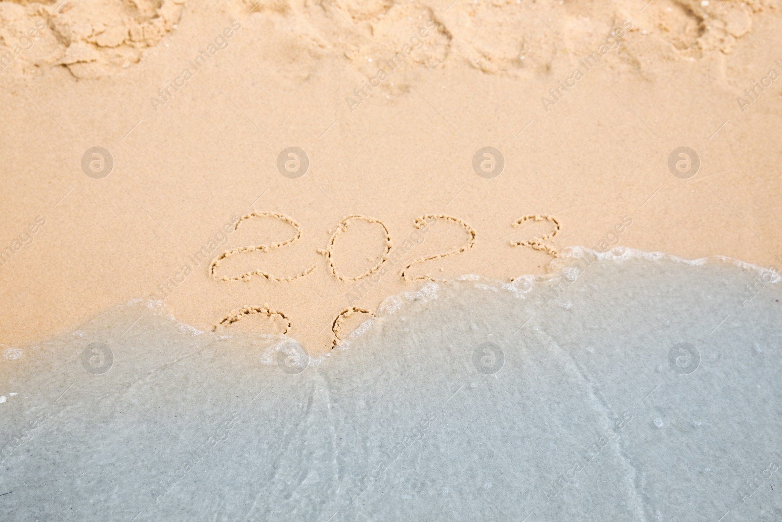 Photo of Dates written on sandy beach. 2022 washed by sea wave as New 2023 Year coming