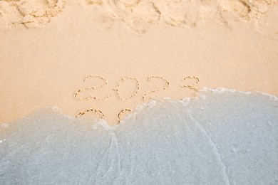 Photo of Dates written on sandy beach. 2022 washed by sea wave as New 2023 Year coming