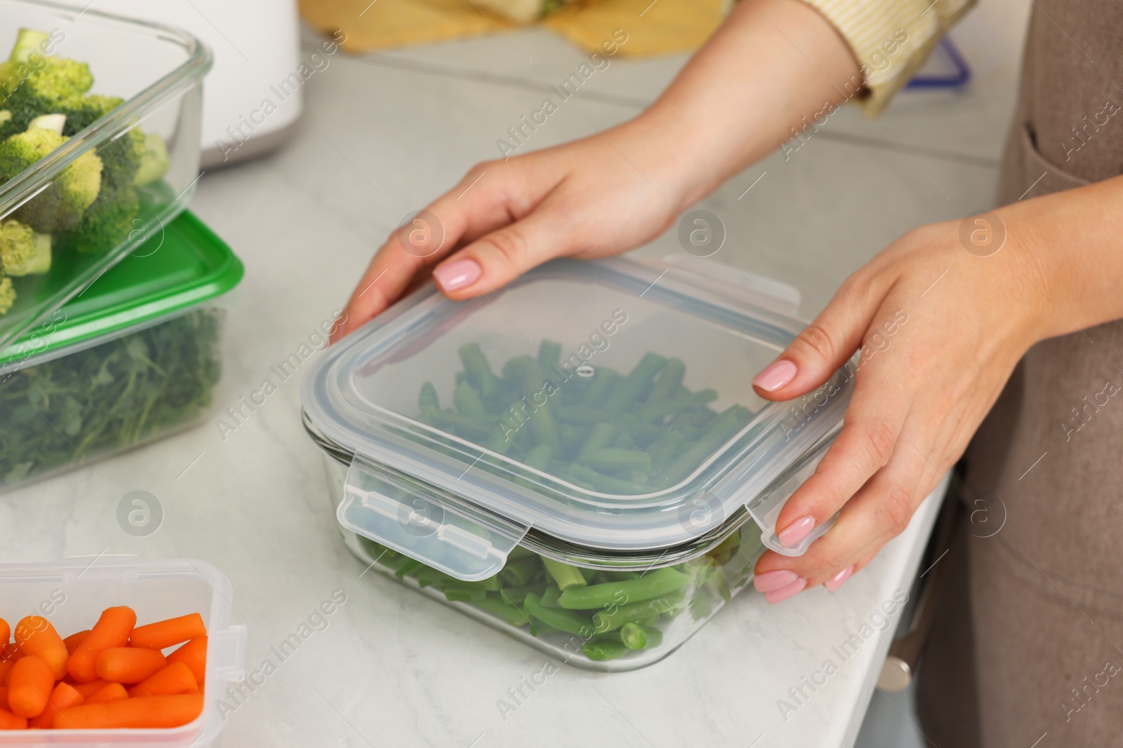 Photo of Woman sealing glass container with lid at white marble table, closeup. Food storage