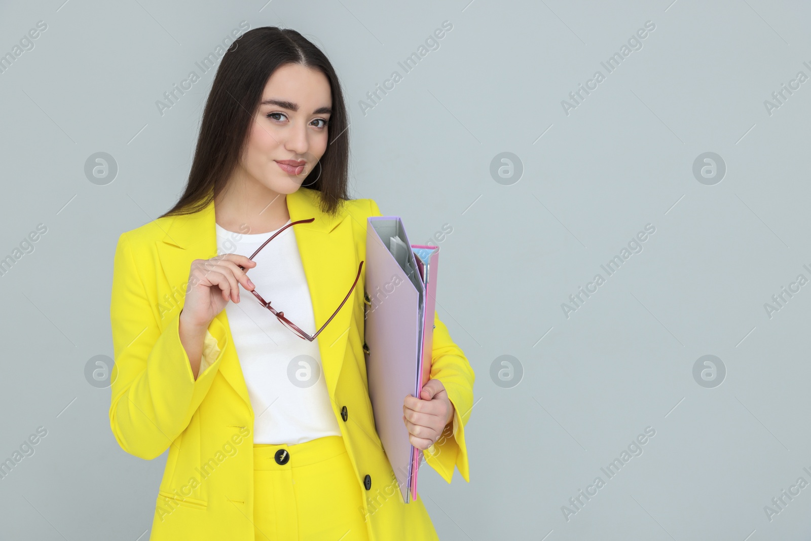 Photo of Young female intern with eyeglasses and folders on grey background, space for text