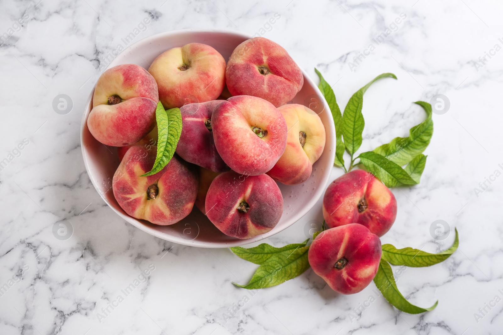 Photo of Fresh ripe donut peaches with leaves on white marble table, flat lay