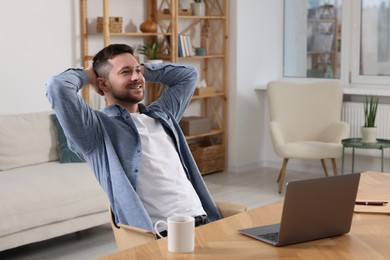 Photo of Happy man having break while working with laptop at wooden desk in room