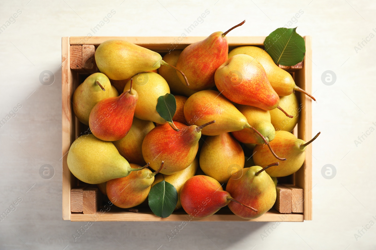 Photo of Wooden crate with ripe pears on light background, top view