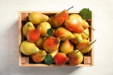 Wooden crate with ripe pears on light background, top view