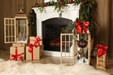 Photo of Beautiful Christmas lanterns and presents near fireplace in room with festive decor