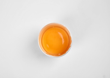 Photo of Cracked raw chicken egg with yolk on white background, top view