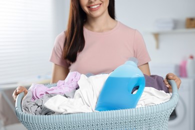 Woman holding basket with dirty clothes and fabric softener in bathroom, closeup