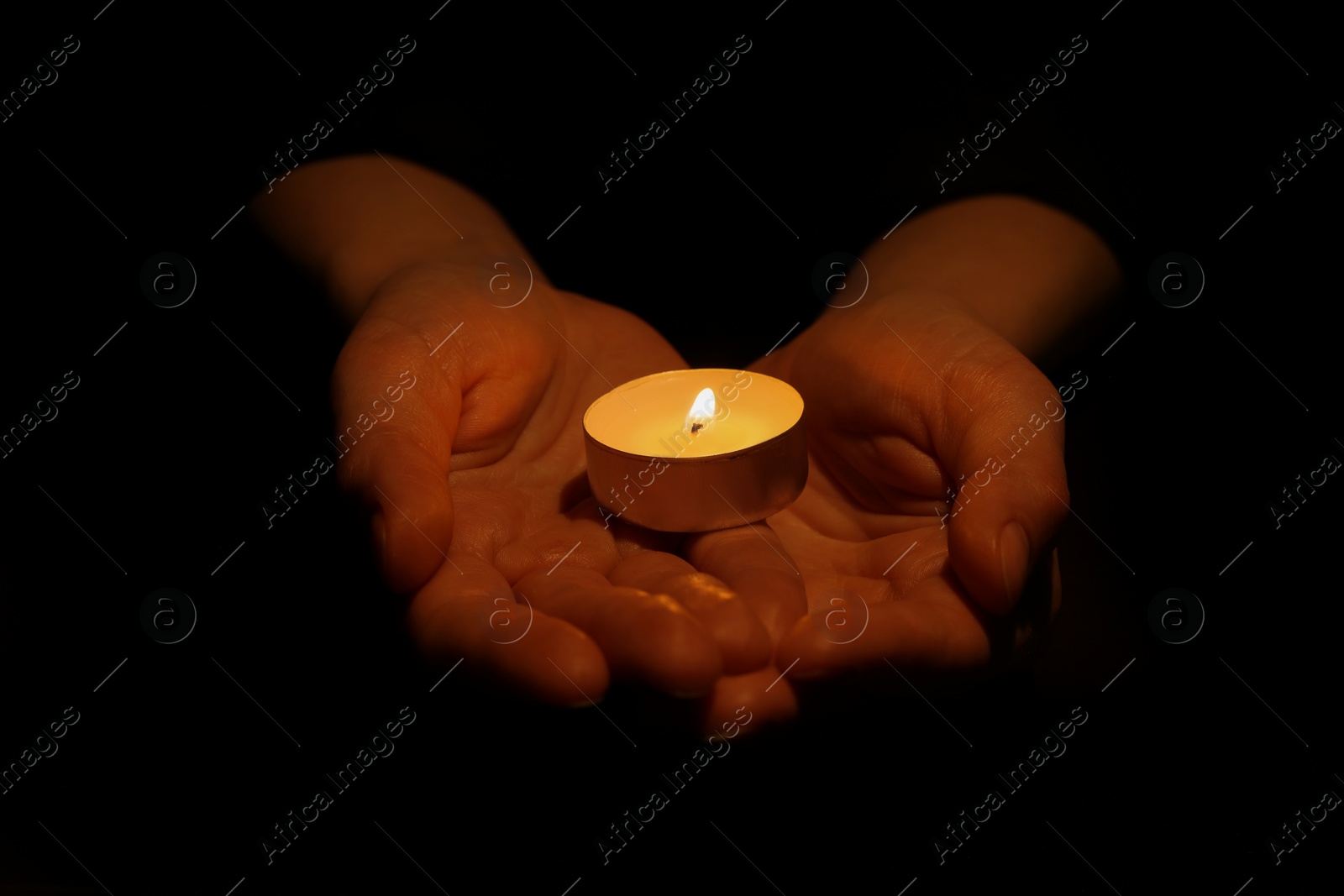 Photo of Woman holding burning candle in hands on black background, closeup