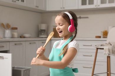 Photo of Cute little girl with headphones and fork spatula singing in kitchen