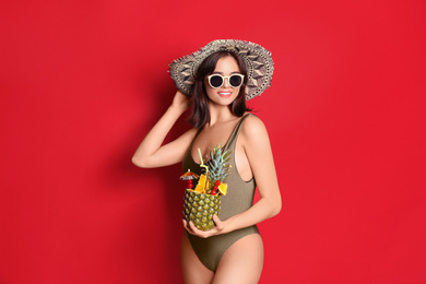 Photo of Beautiful woman in stylish swimsuit holding tropical cocktail on red background