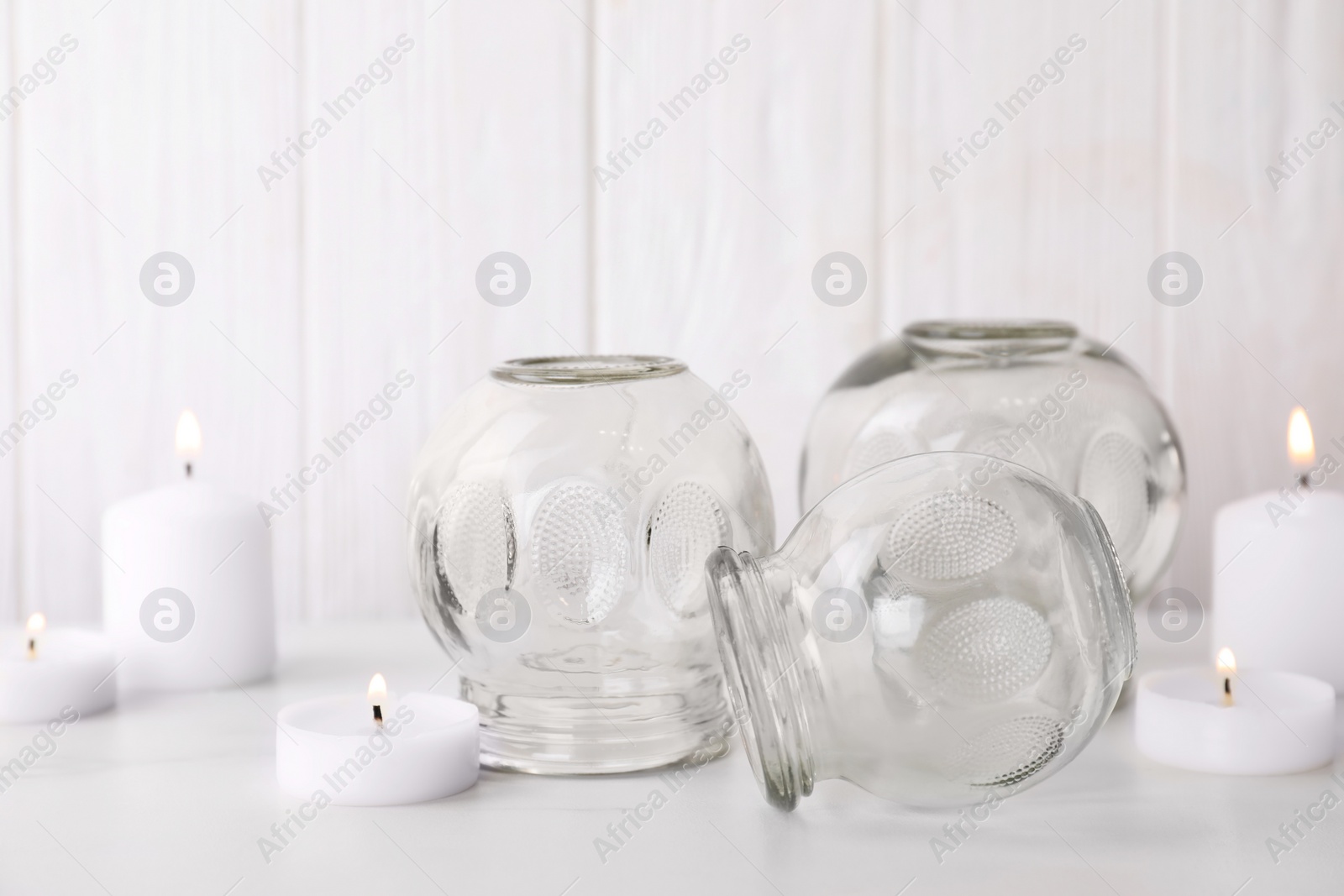 Photo of Glass cups and burning candles on white table. Cupping therapy