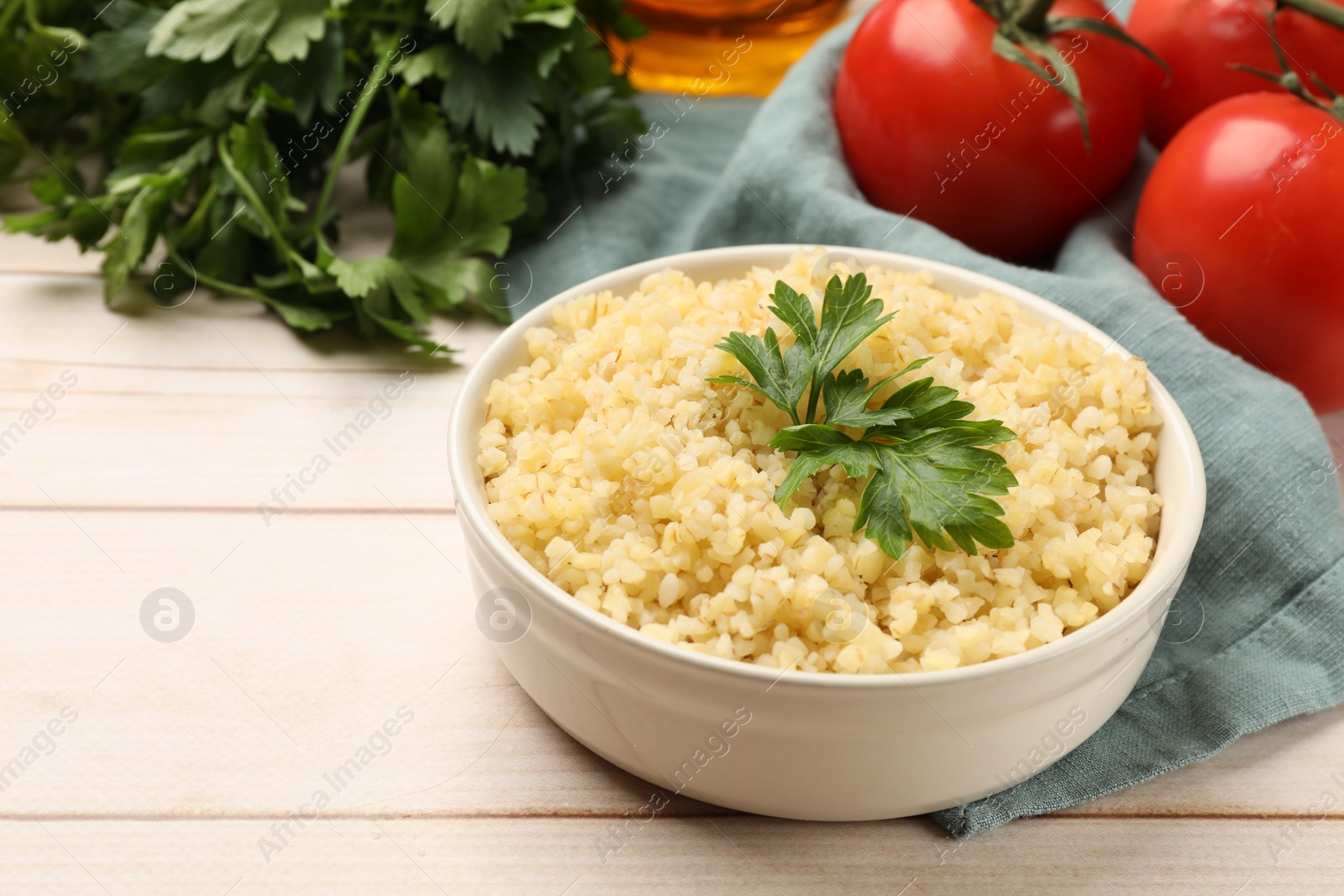 Photo of Delicious bulgur with parsley in bowl and tomatoes on wooden table, closeup