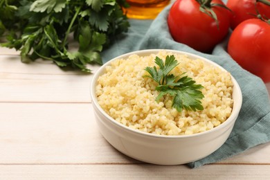 Delicious bulgur with parsley in bowl and tomatoes on wooden table, closeup